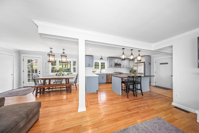 living room featuring light wood-style floors, baseboards, ornamental molding, and visible vents