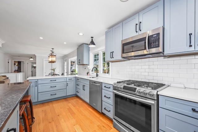 kitchen with a peninsula, a sink, light wood finished floors, appliances with stainless steel finishes, and backsplash