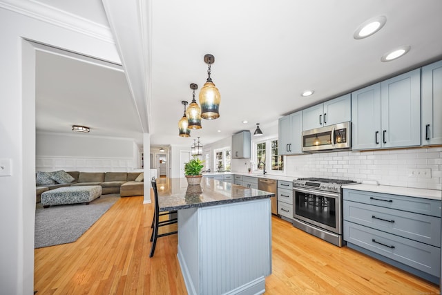 kitchen with a kitchen breakfast bar, gray cabinets, tasteful backsplash, light wood-style flooring, and stainless steel appliances