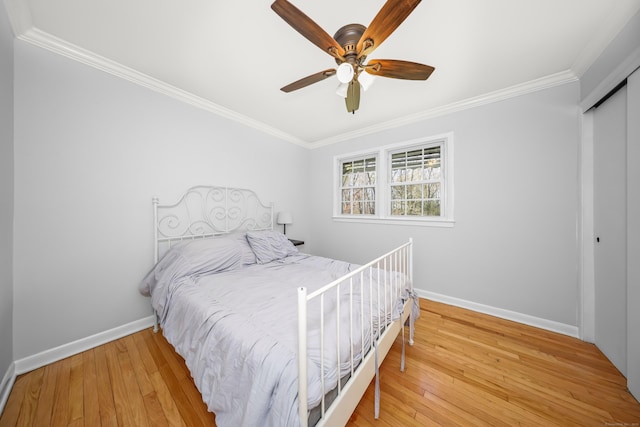 bedroom with ceiling fan, crown molding, baseboards, wood-type flooring, and a closet