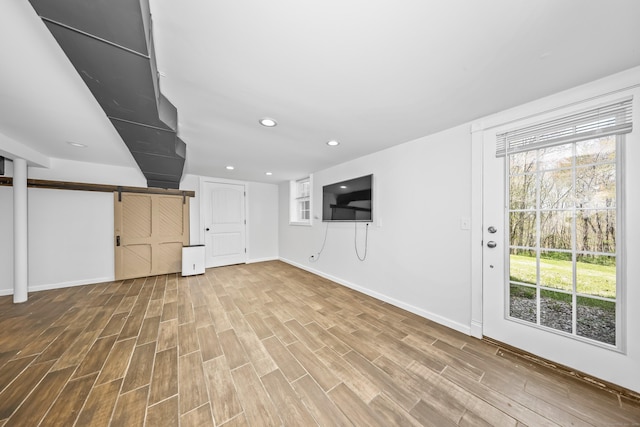 unfurnished living room featuring recessed lighting, baseboards, a barn door, and wood finished floors