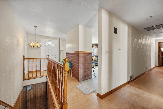 corridor with plenty of natural light, a textured wall, visible vents, and an upstairs landing