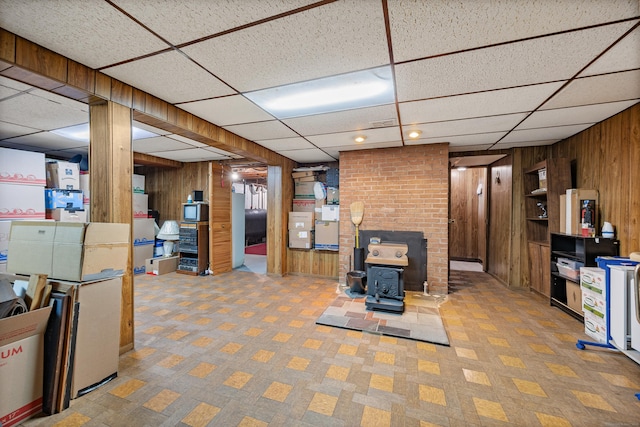 finished basement featuring wood walls, a paneled ceiling, and a wood stove