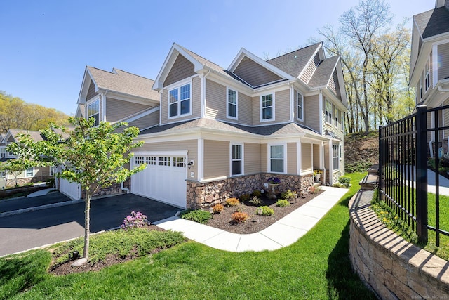 view of front of house featuring a front lawn, fence, stone siding, a shingled roof, and driveway