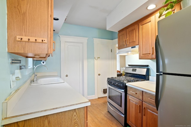 kitchen with light wood-type flooring, light countertops, under cabinet range hood, a sink, and stainless steel appliances