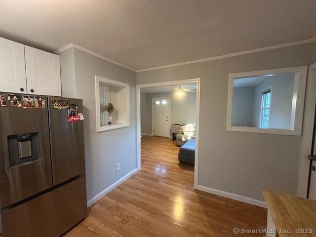 hallway with light wood-style floors, ornamental molding, and baseboards