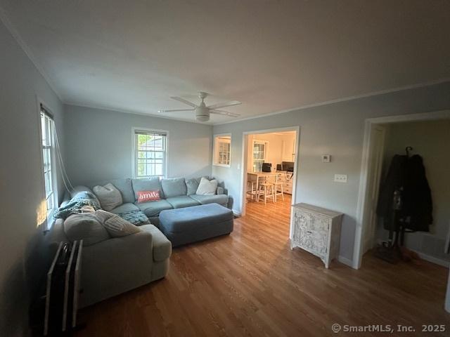 living area with a ceiling fan, baseboards, ornamental molding, and wood finished floors