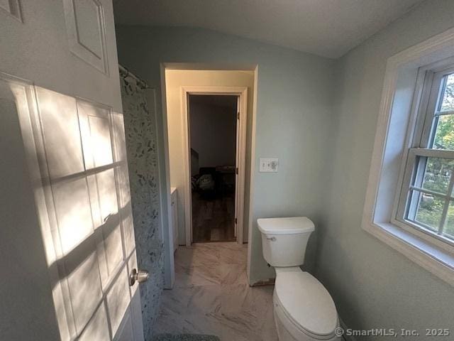 bathroom with marble finish floor, vaulted ceiling, toilet, and a wealth of natural light