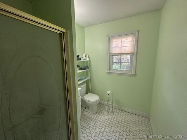 bathroom featuring toilet, baseboards, and a stall shower