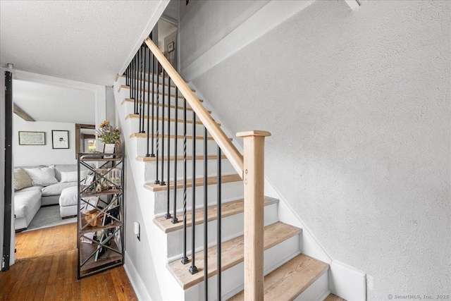 stairway with a textured ceiling, a textured wall, and wood finished floors