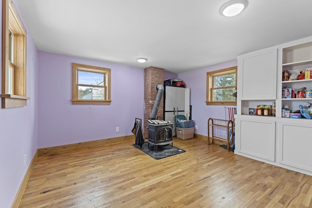 recreation room with baseboards, light wood-style flooring, and a wood stove
