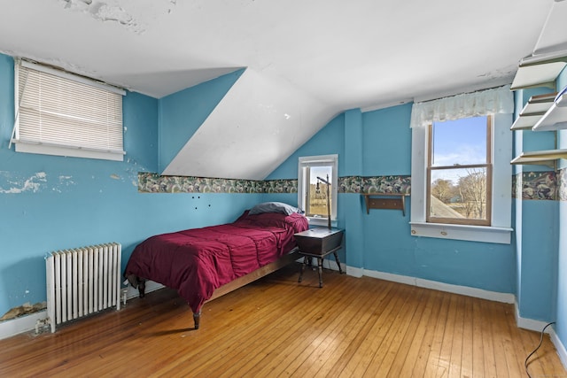 bedroom featuring baseboards, lofted ceiling, radiator, and hardwood / wood-style floors