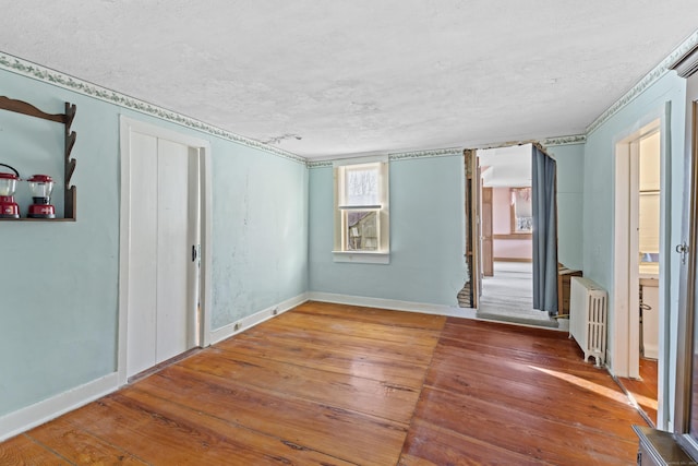 unfurnished room with radiator, baseboards, wood-type flooring, and a textured ceiling