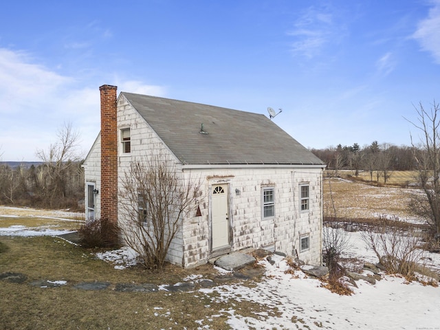 snow covered rear of property with roof with shingles and a chimney