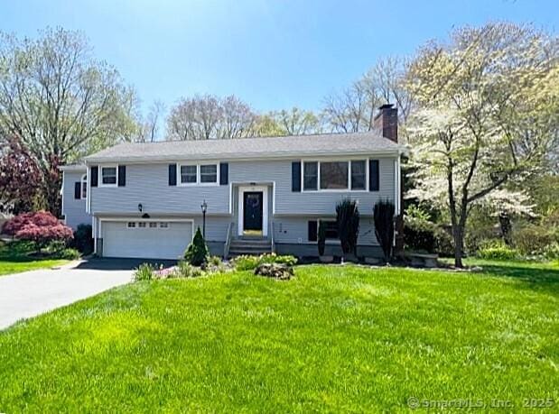 split foyer home with driveway, a chimney, a front yard, and a garage