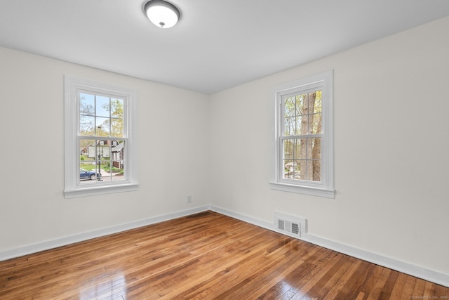 empty room featuring visible vents, baseboards, a healthy amount of sunlight, and hardwood / wood-style floors