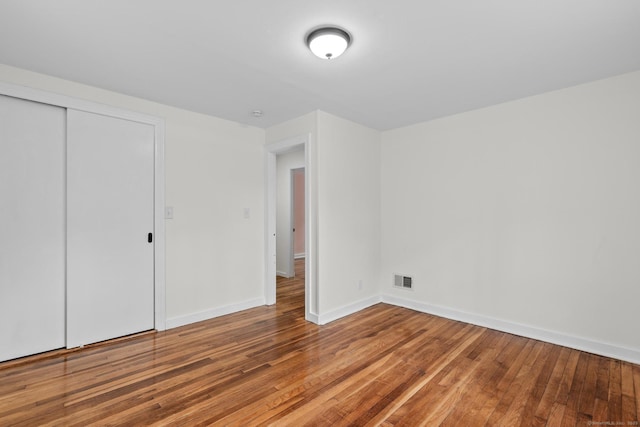 unfurnished bedroom featuring baseboards, a closet, visible vents, and hardwood / wood-style flooring