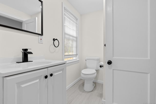 half bath featuring baseboards, toilet, and vanity