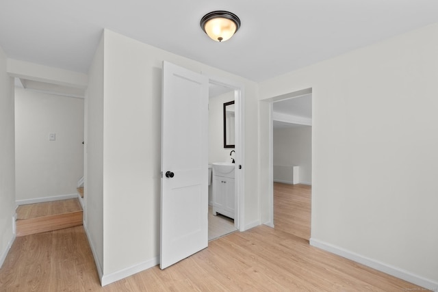 spare room featuring light wood-style floors, a sink, and baseboards