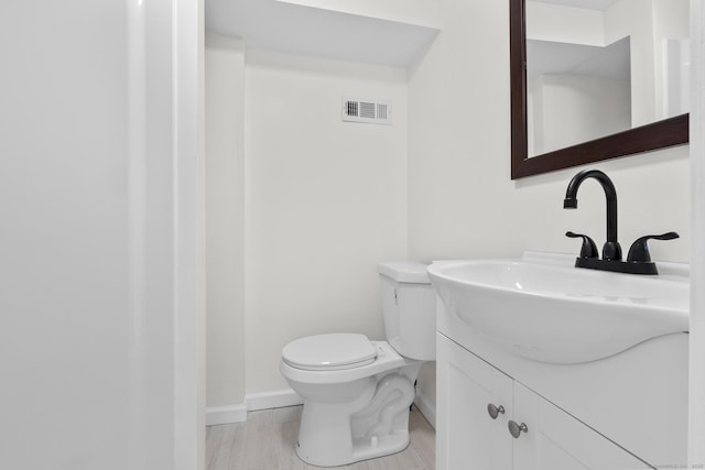 half bathroom with visible vents, vanity, wood finished floors, toilet, and baseboards