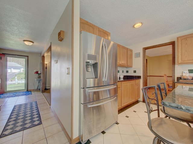 kitchen with stainless steel fridge with ice dispenser, light brown cabinets, a textured ceiling, dark stone counters, and light tile patterned floors