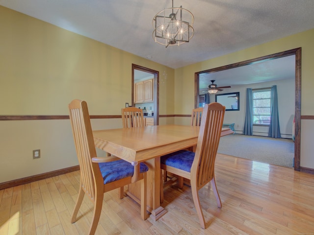 dining space with baseboards, a baseboard heating unit, ceiling fan with notable chandelier, and light wood-style floors