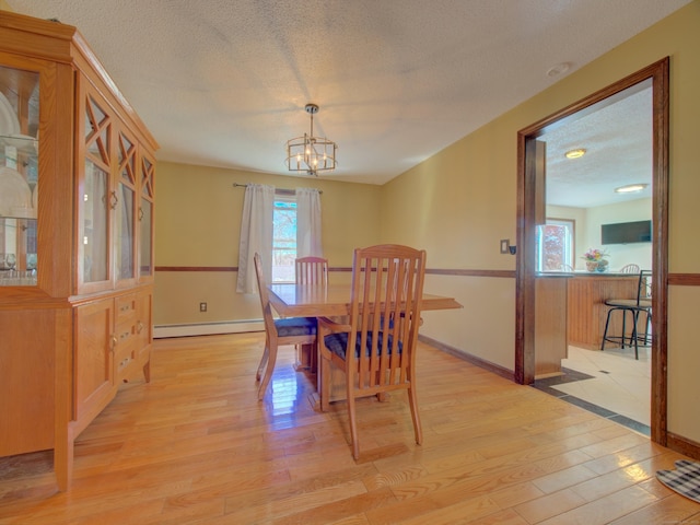 dining room with an inviting chandelier, baseboard heating, a textured ceiling, baseboards, and light wood-type flooring