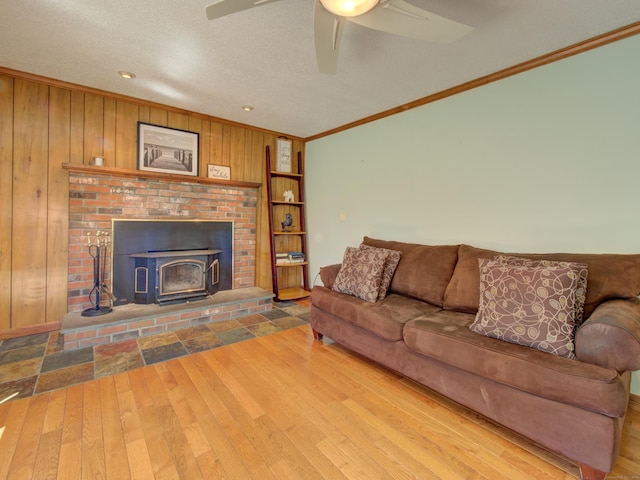 living room featuring ornamental molding, wood walls, a wood stove, wood finished floors, and ceiling fan