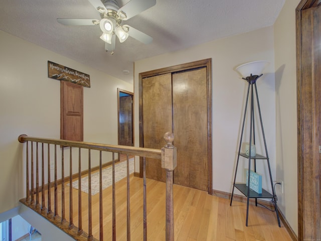 hall featuring baseboards, a textured ceiling, an upstairs landing, and light wood-style flooring