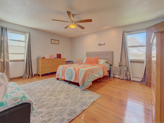 bedroom featuring a textured ceiling, light wood-style flooring, ceiling fan, and baseboard heating