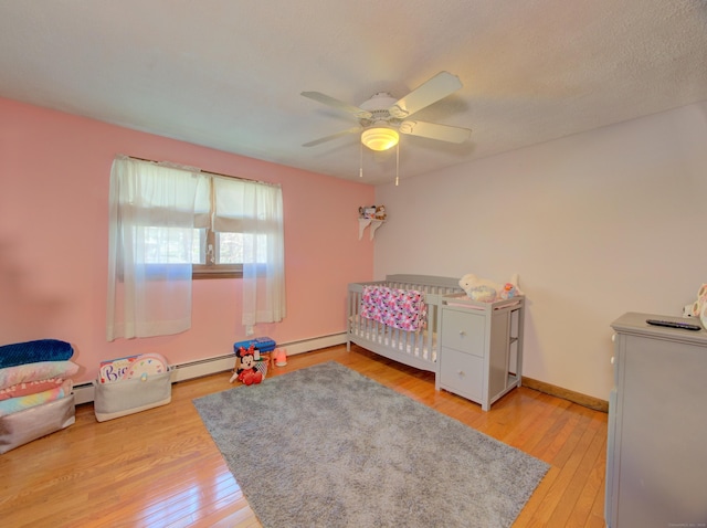 bedroom featuring a crib, baseboards, a ceiling fan, and light wood finished floors