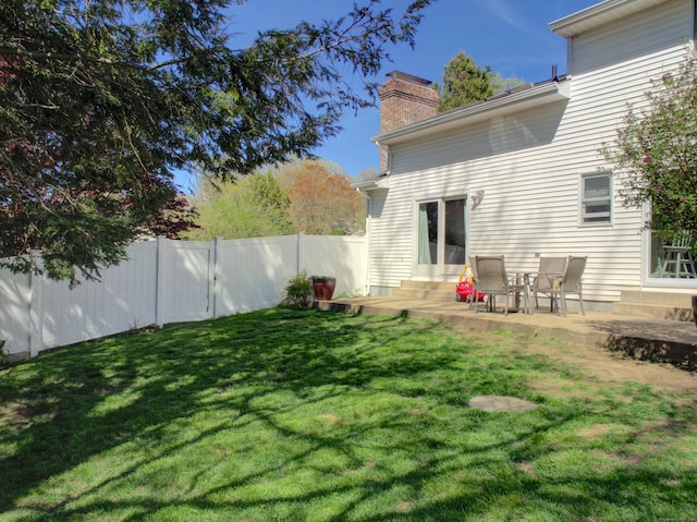 rear view of house featuring fence, entry steps, a chimney, a patio, and a yard