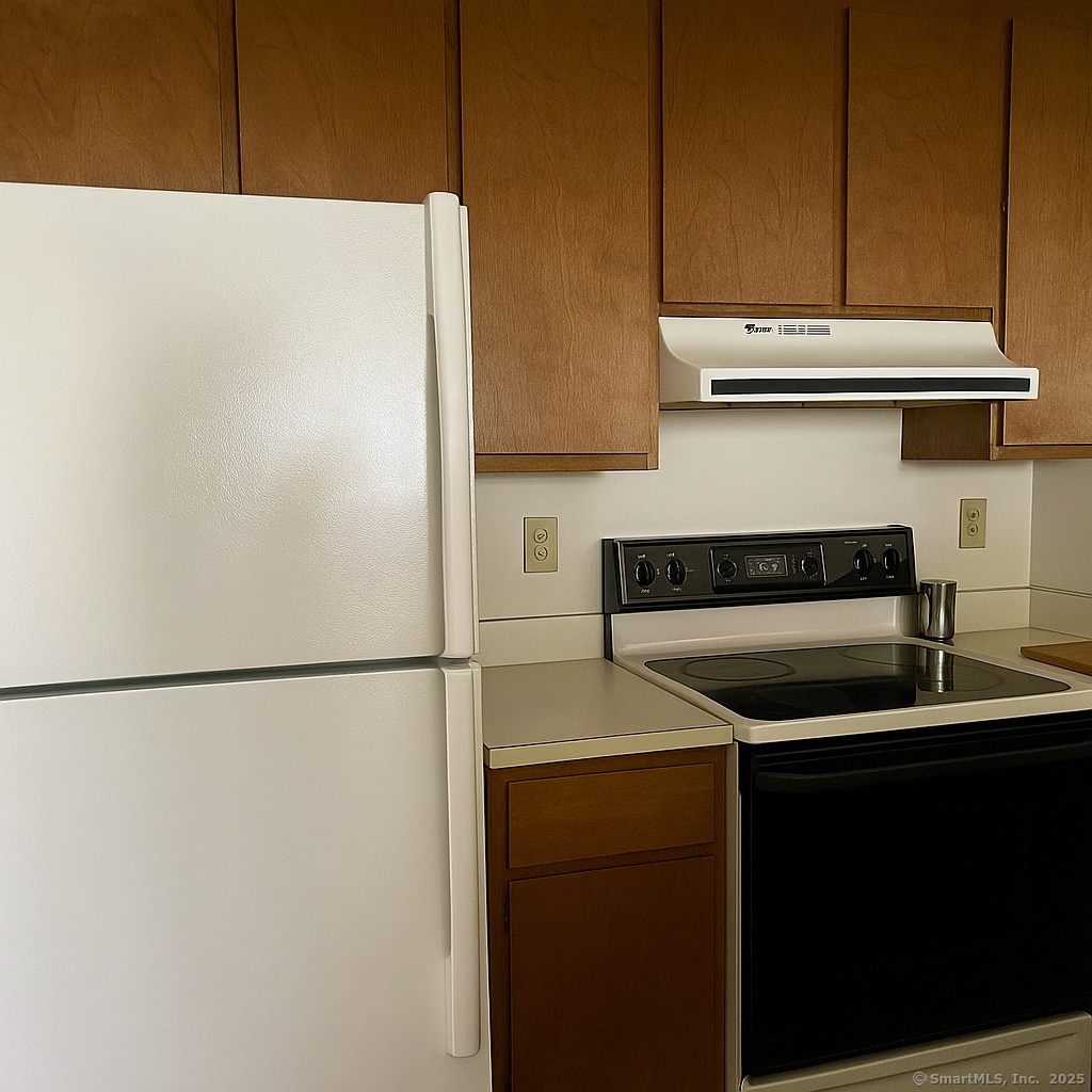 kitchen featuring range with electric stovetop, freestanding refrigerator, ventilation hood, and light countertops