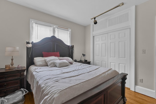 bedroom featuring baseboards, light wood finished floors, a closet, and track lighting