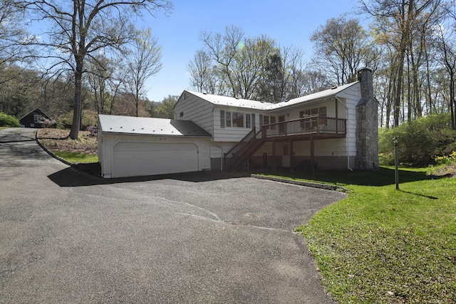 view of front of house with an attached garage, a front lawn, stairway, a chimney, and driveway