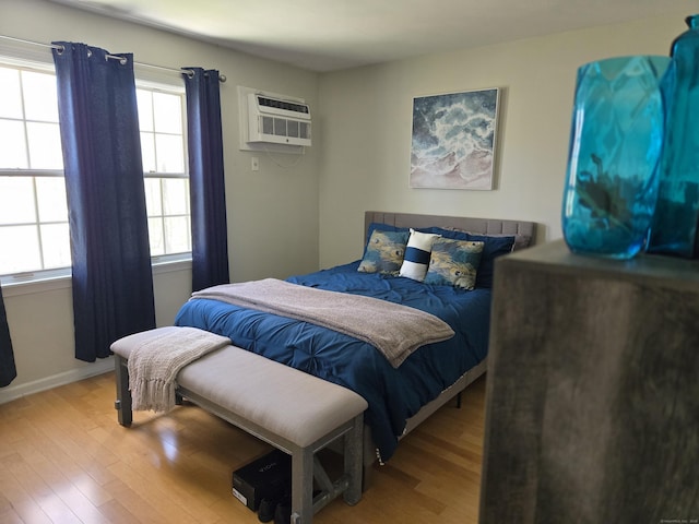 bedroom with an AC wall unit, baseboards, and wood finished floors