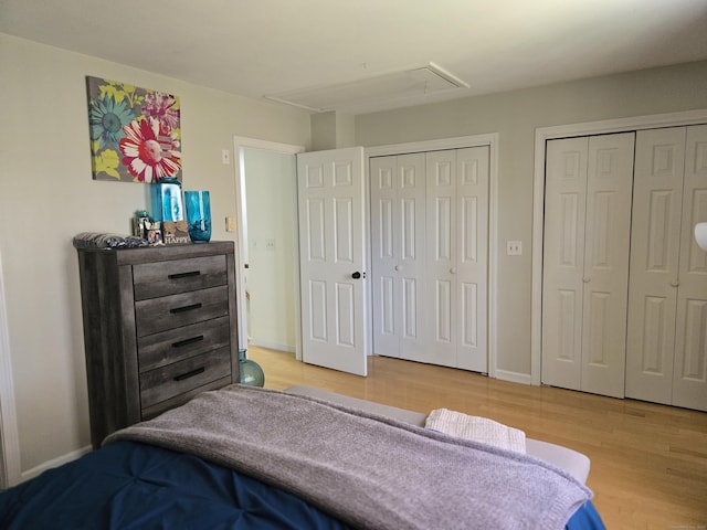 bedroom with baseboards, attic access, multiple closets, and light wood-style flooring