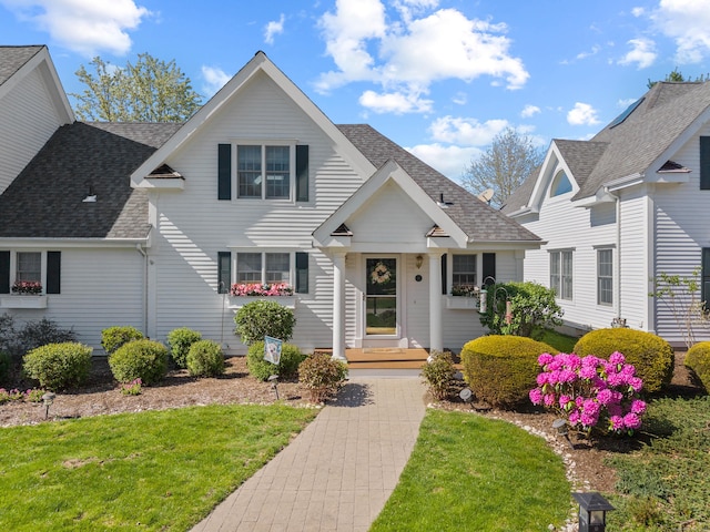 traditional-style home featuring roof with shingles and a front lawn