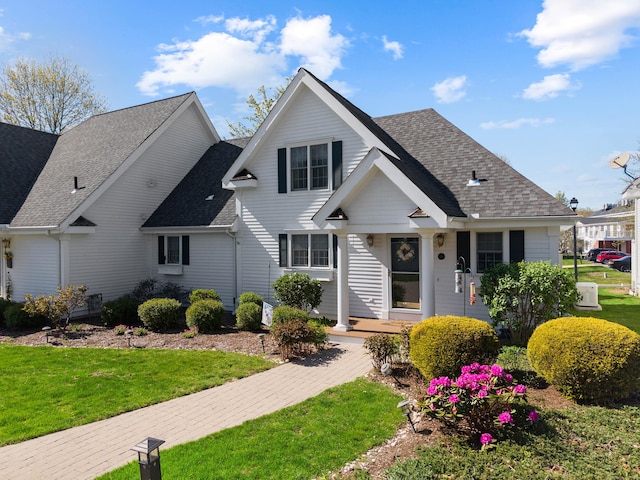 traditional-style house with a front lawn, roof with shingles, and covered porch