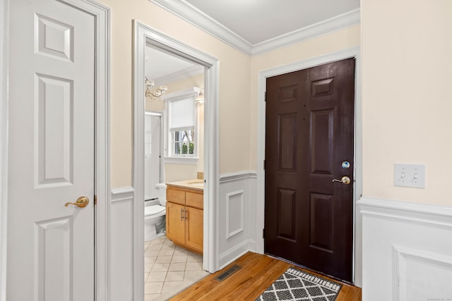 entrance foyer with ornamental molding, wainscoting, and visible vents