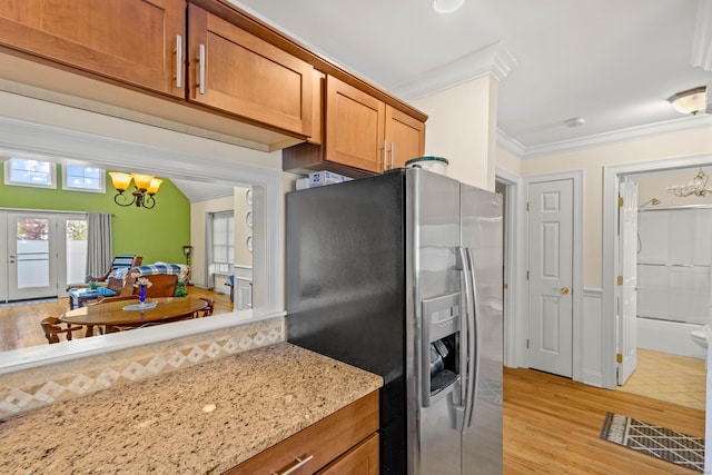 kitchen with an inviting chandelier, crown molding, light stone countertops, brown cabinets, and stainless steel fridge with ice dispenser