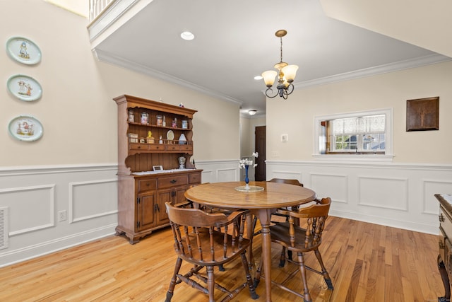 dining space featuring crown molding, a wainscoted wall, an inviting chandelier, and light wood-style floors