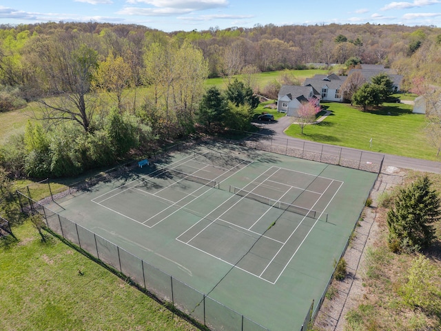 view of sport court featuring fence, a view of trees, and a yard