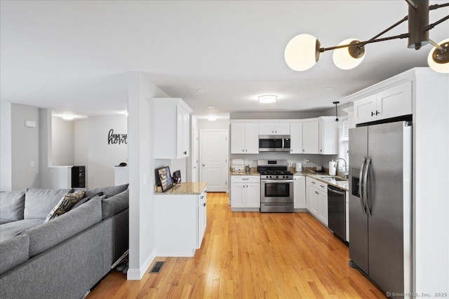 kitchen with a sink, open floor plan, stainless steel appliances, white cabinets, and light wood-type flooring