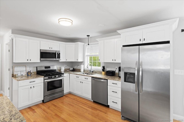 kitchen with a sink, stainless steel appliances, white cabinetry, and light stone countertops