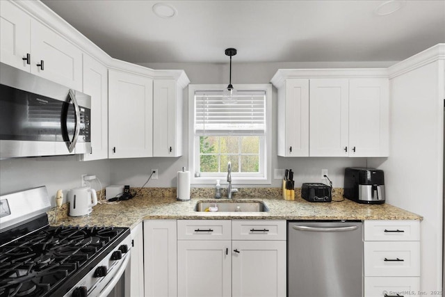 kitchen with hanging light fixtures, light stone counters, a sink, white cabinetry, and stainless steel appliances