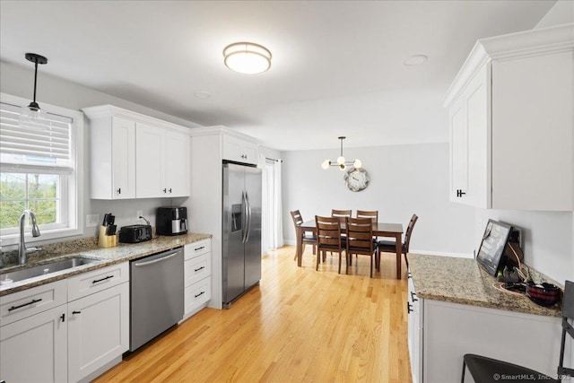kitchen featuring light wood-style flooring, a sink, stainless steel appliances, white cabinetry, and light stone countertops