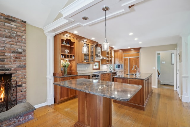 50 Carriage Dr S, Stamford, CT 06902 - kitchen featuring a center island with sink, brown cabinets, built in appliances, wall chimney range hood, and decorative columns