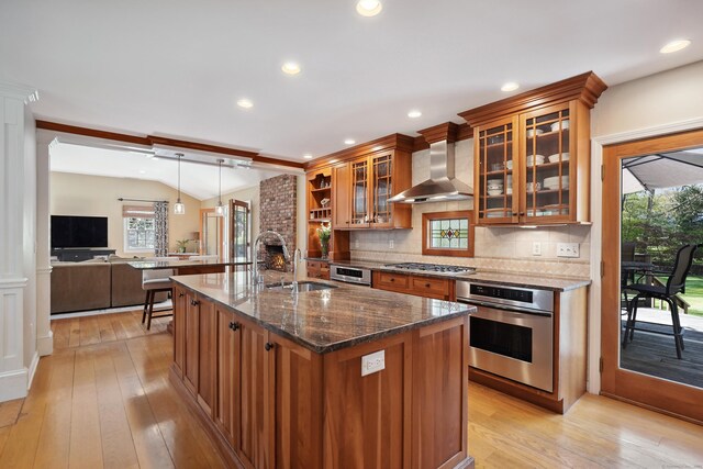 50 Carriage Dr S, Stamford, CT 06902 - kitchen featuring appliances with stainless steel finishes, wall chimney range hood, a sink, brown cabinetry, and light wood-type flooring