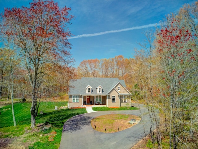 cape cod-style house with curved driveway, covered porch, and a front yard